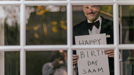 Man in window holding happy birthday sign